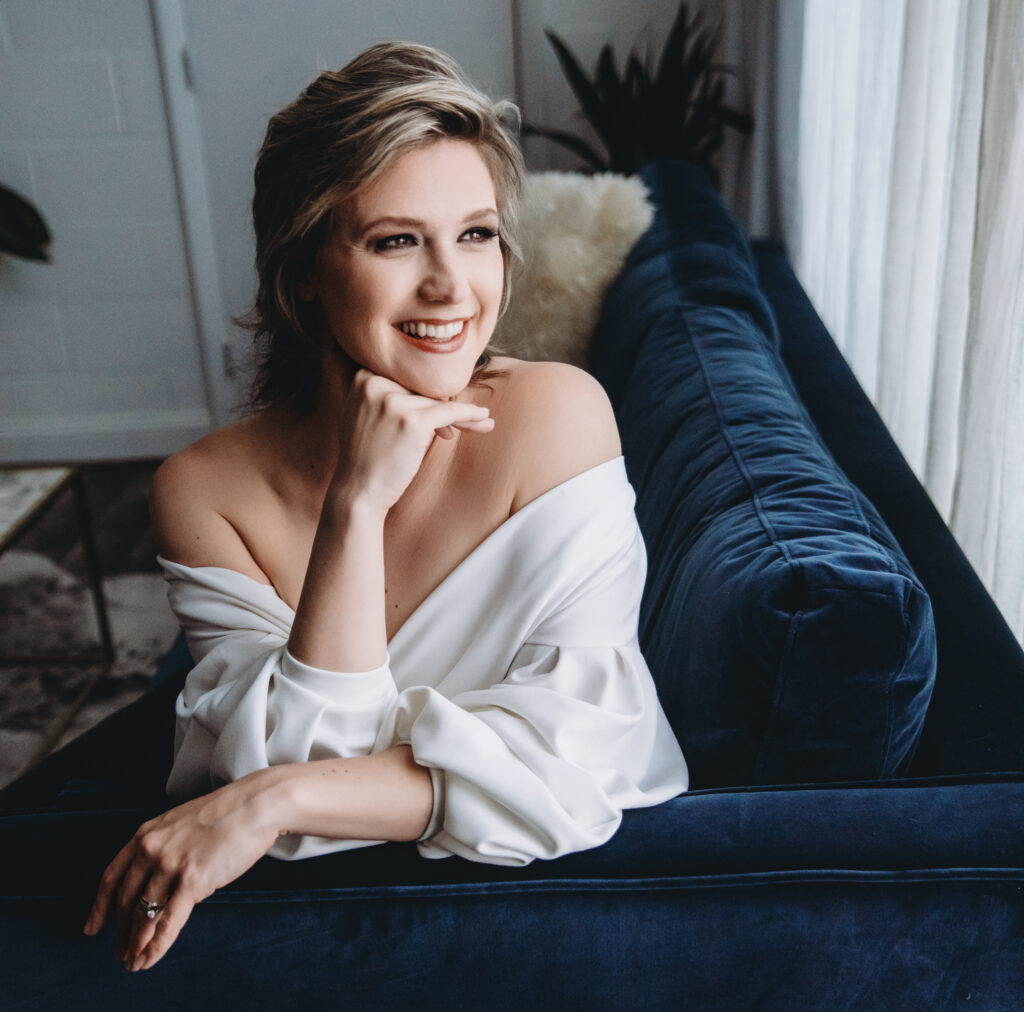 Show your Spark owner and photography Lindsay Hite in a white blouse sitting on a navy sofa with a white backdrop.