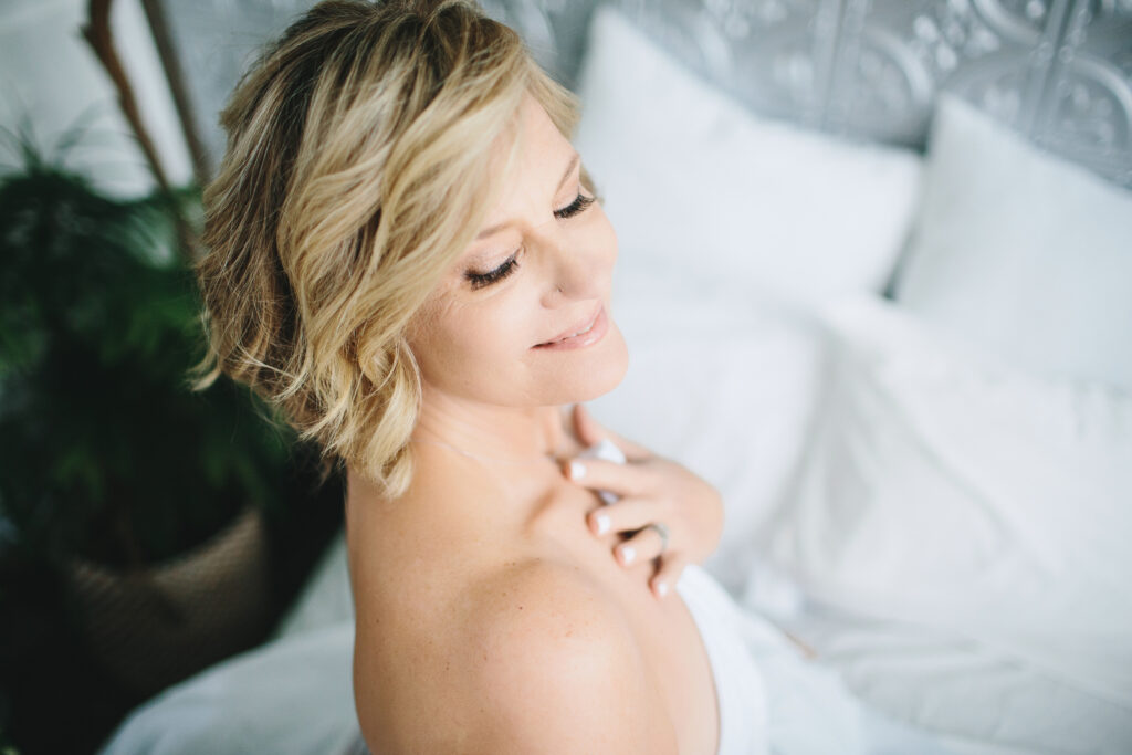 Woman sitting up in white sheets. Photography by Lindsay Hite