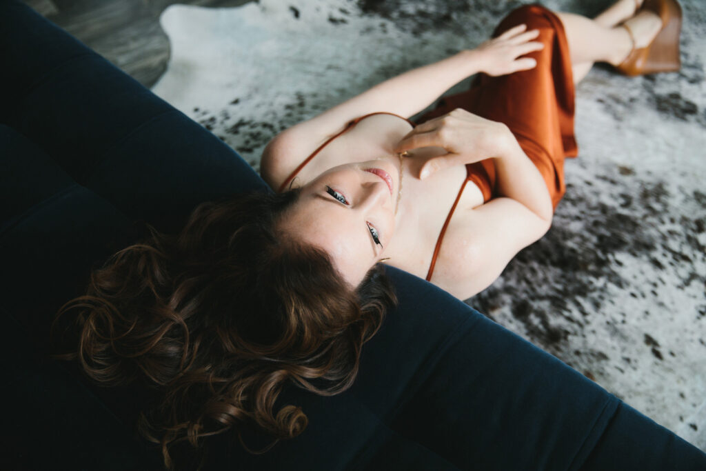 Woman in rust colored dress leaning on a blue sofa. Photography by Lindsay Hite