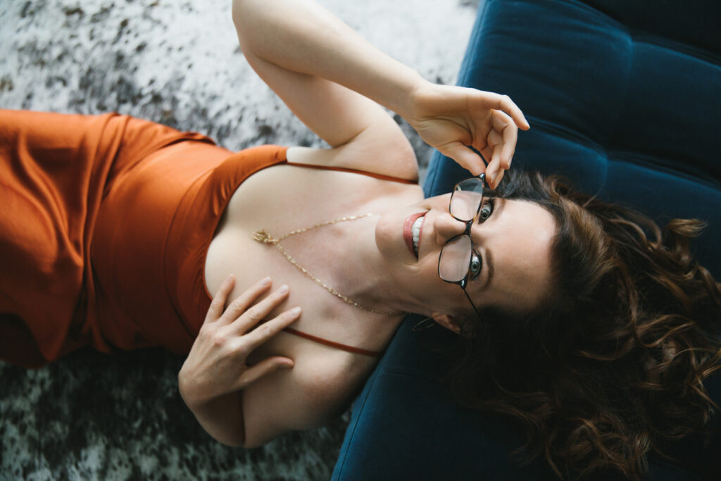 Woman in rust colored dress leaning on a blue sofa. Photography by Lindsay Hite