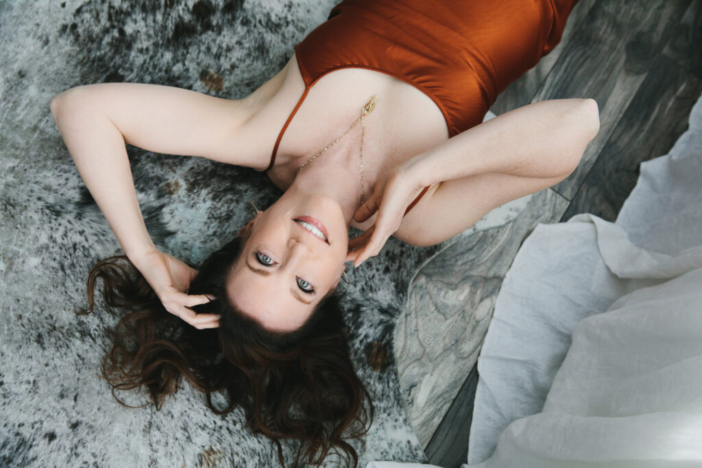 Woman in rust colored dress laying on the floor using photography as a tool for self-discovery and empowerment. Photography by Lindsay Hite