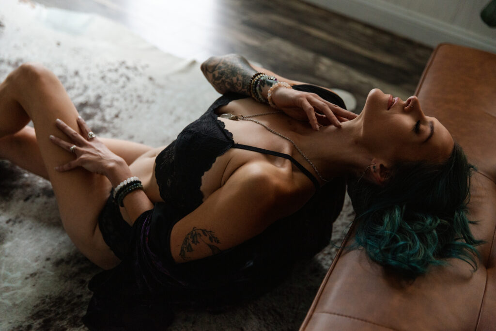 Woman in black lingerie sitting on the floor leaning back against a leather sofa. Photography by Lindsay Hite. 