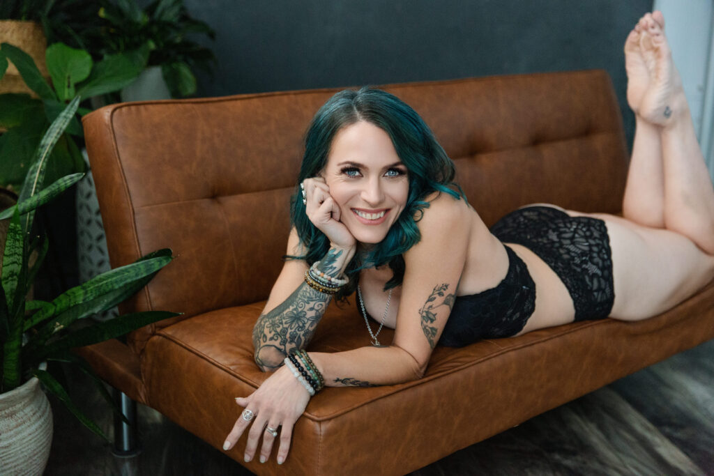 Woman in black lingerie on her belly on a leather sofa looking directly at the camera.  Photography by Lindsay Hite. 