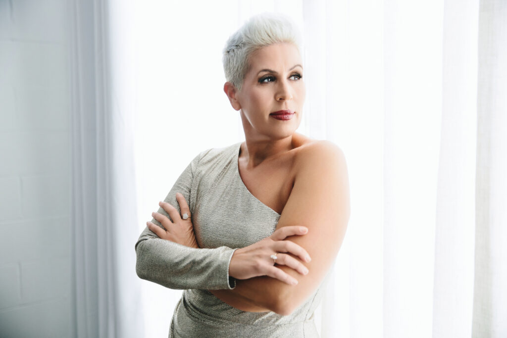 Woman in silver dress against white curtains.  Photography by Lindsay Hite