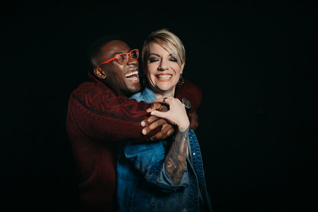 Couple celebrating their relationship with laughter and love through photography against a black backdrop.  Photography by Lindsay Hite