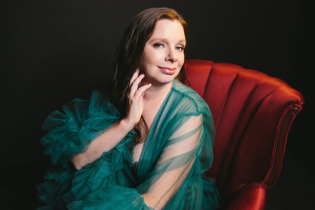 Woman in teal robe sitting on a red velvet chair.  Photography Lindsay Hite