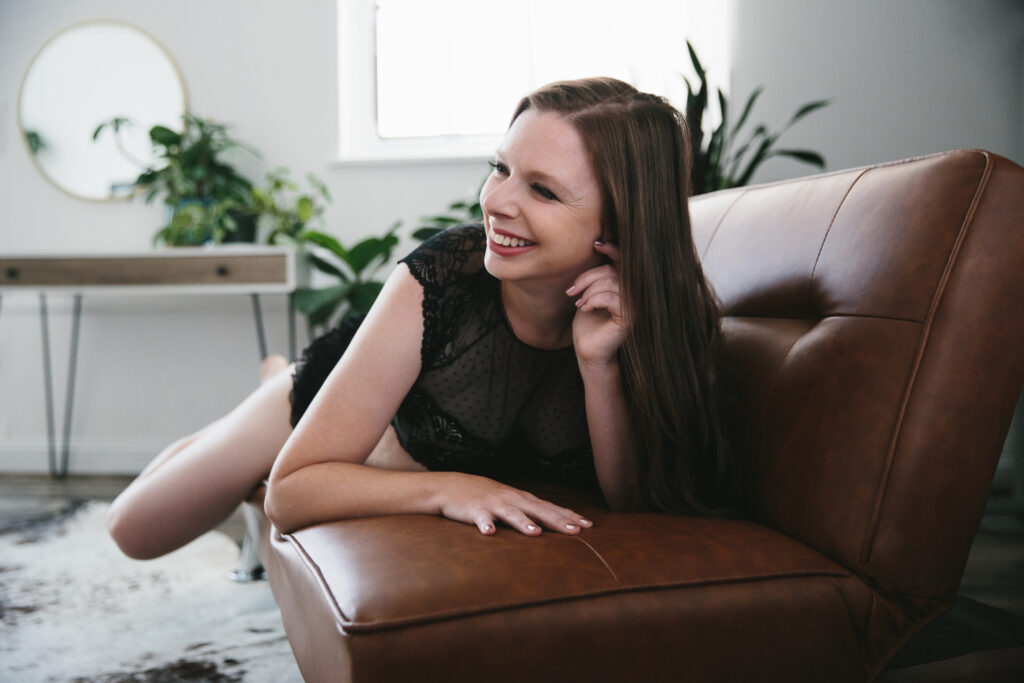 Woman in black lingerie laying on her belly on a tan sofa happy after discovering her why.  Photography Lindsay Hite