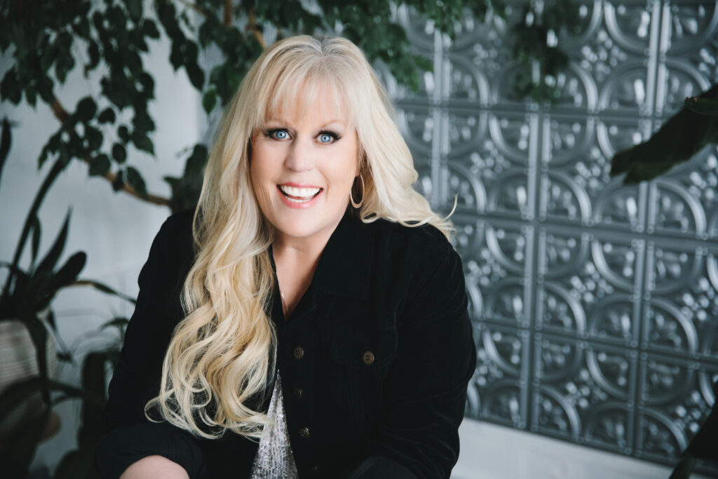 Woman in a silver sparkly top and black blazer smiling at the camera. Photography by Lindsay Hite.