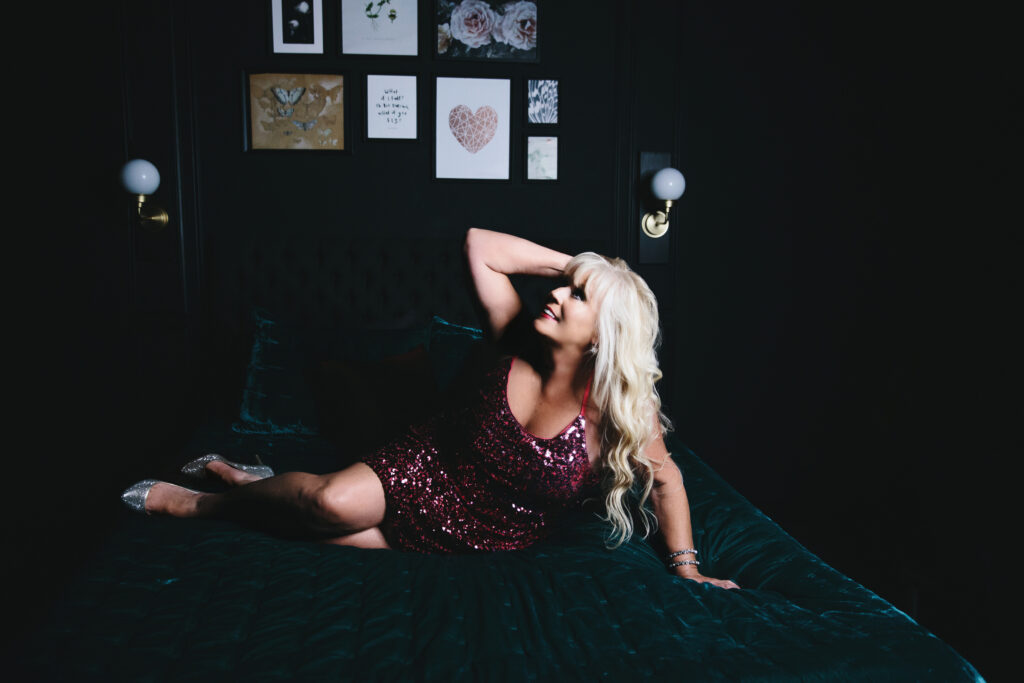 A woman in a pink silver sequence dress lying on a jewel-toned bed. Photography by Lindsay Hite.
