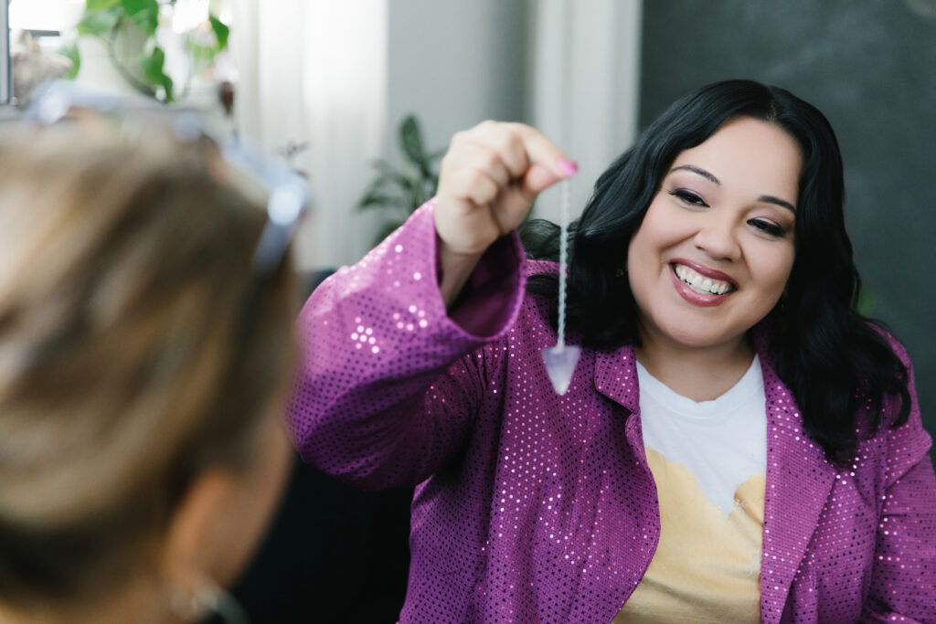 Woman wearing a purple sparkle jacket holding a crystal up in the air while working with a client. Photography by Lindsay Hite