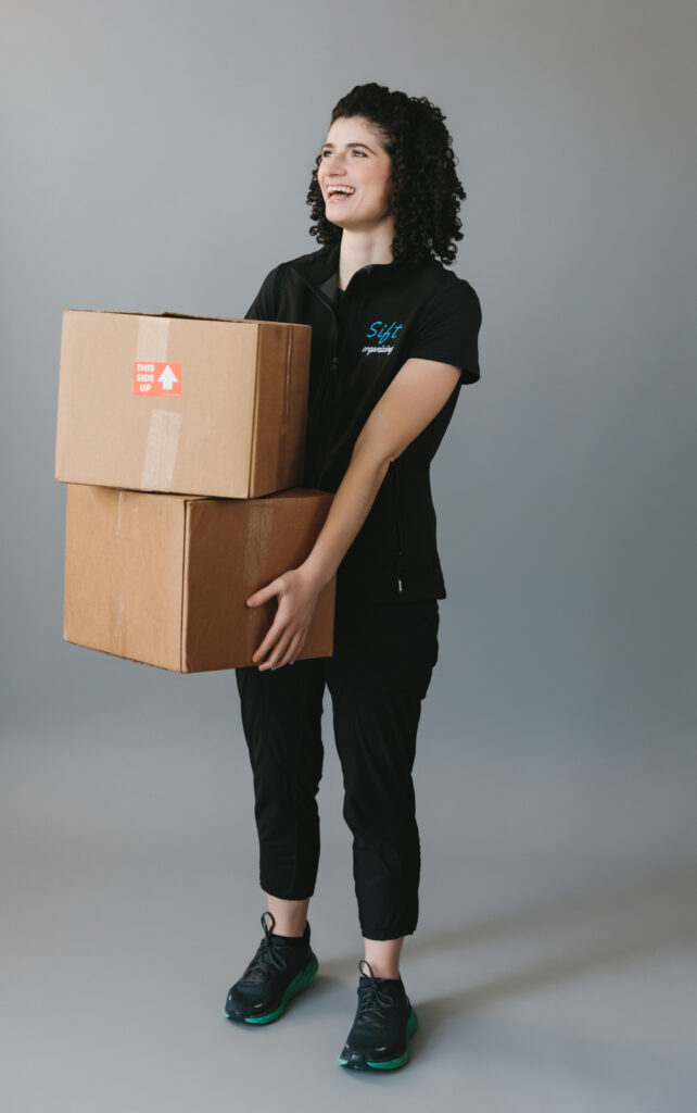 Woman wearing a company shirt holding moving boxes with a neutral background. Photography by Lindsay Hite