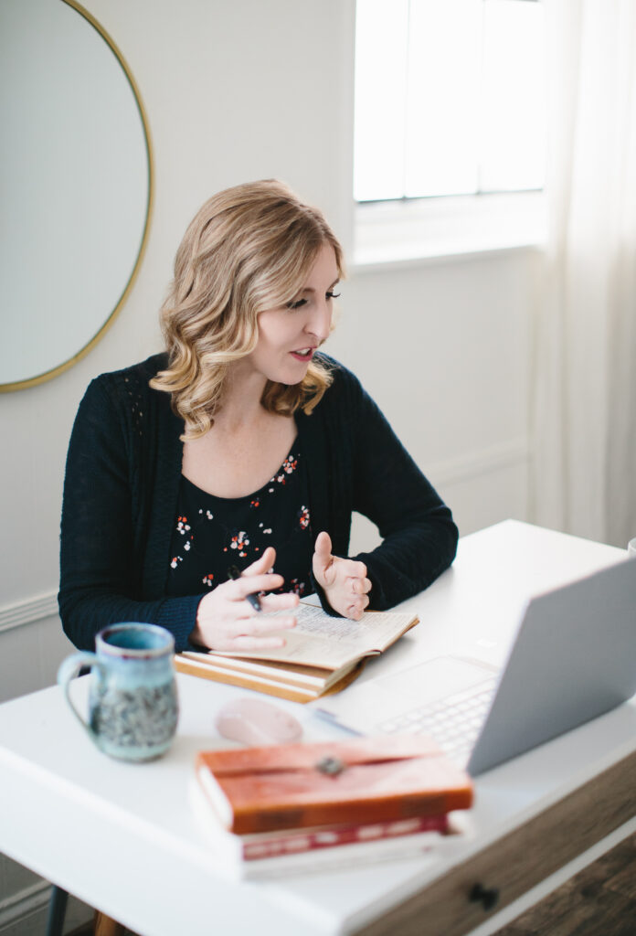 Woman in a navy top and cardigan sitting at a desk, with a journal in front of her, in a virtual meeting. Photography by Lindsay Hite