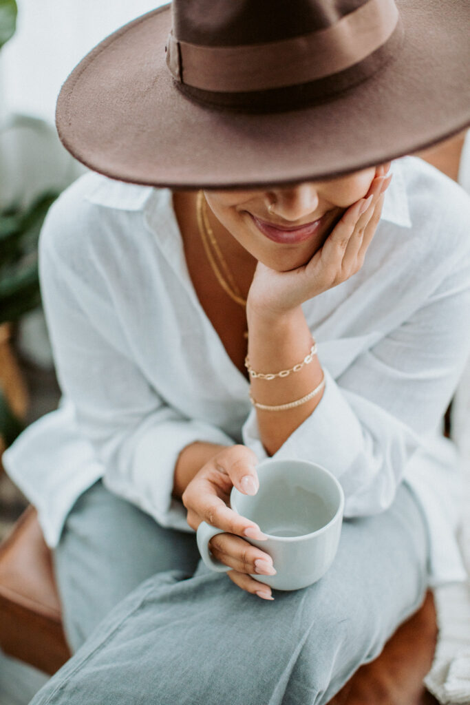 A woman earing a hat and holding a coffee cup. Photography by Lindsay Hite