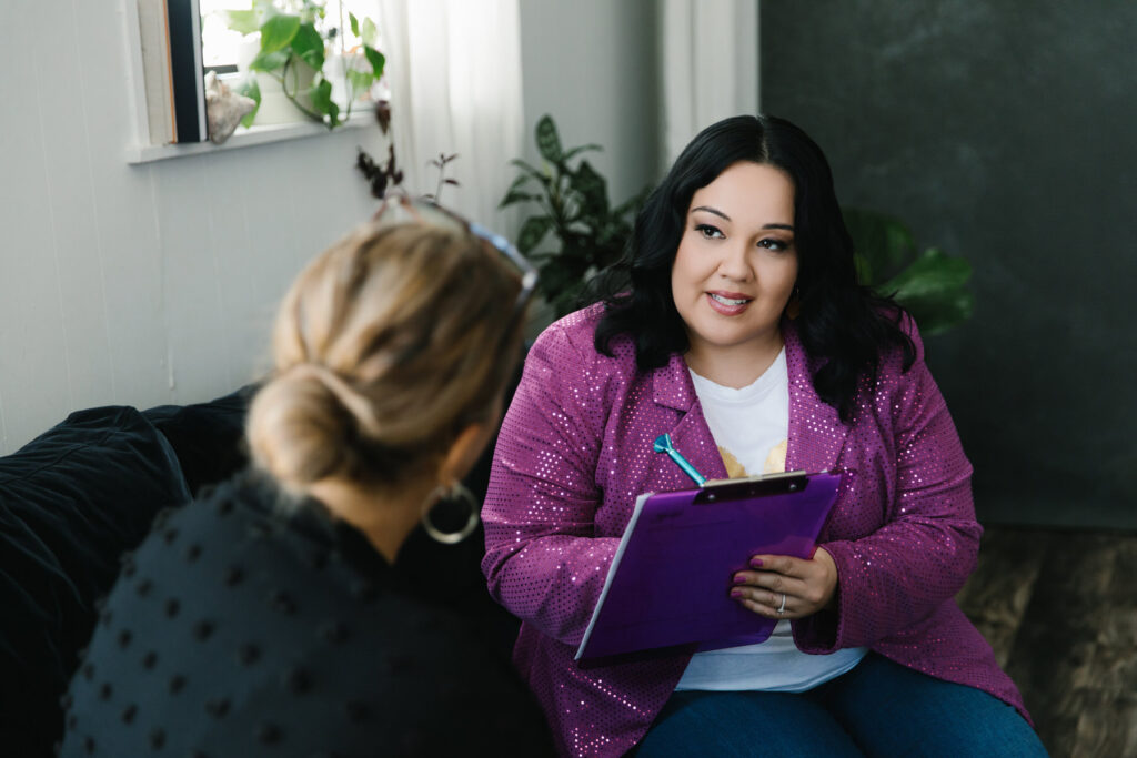Woman in purple blazer sitting on the couch with a client in a session. Photography by Lindsay Hite